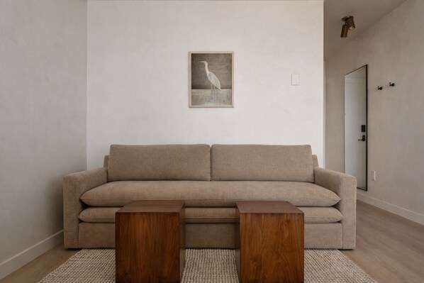 A neutral-toned sofa with two wooden side tables, a framed picture of a bird on the wall, and a door to the right. - The Herondale Hotel (Astoria)