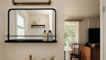 A bathroom with a mirror, a sink, a faucet, a vase with flowers, and a shelf with toiletries.