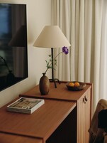 Un escritorio de madera con una lámpara, un florero con una planta, un cuenco con fruta y una revista.