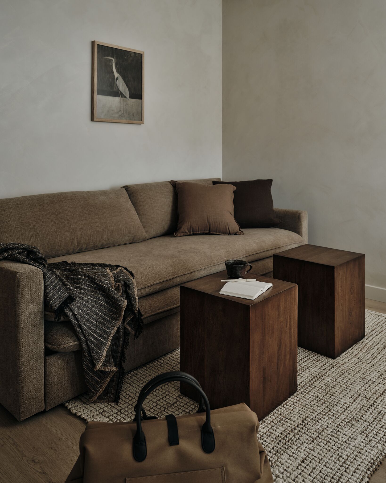 A modern living room with a sofa, two wooden side tables, a coffee table, a brown handbag, and a framed picture on the wall.