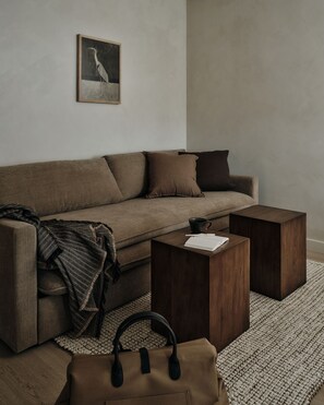 A modern living room with a sofa, two wooden side tables, a coffee table, a brown handbag, and a framed picture on the wall. - The Herondale Hotel (Astoria)