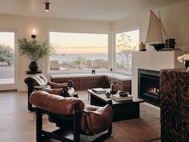 Una sala de estar acogedora con un ventanal grande, mobiliario de cuero, chimenea y un modelo de velero.