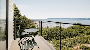 Un balcon avec une table et des chaises, donnant sur une étendue d’eau et sur une terre lointaine.