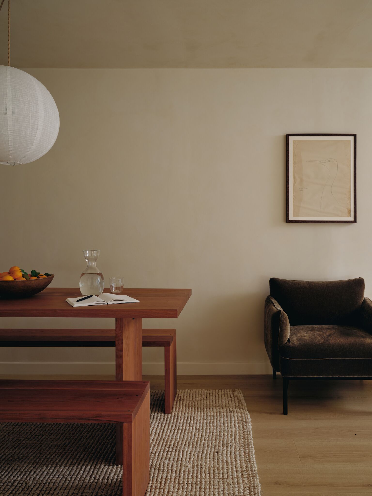 Un salón minimalista con una mesa de madera, un sillón de cuero marrón, un tapiz tejido y un cuadro enmarcado en la pared.