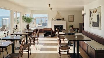 A spacious dining area with multiple tables and chairs, a fireplace, and a large window offering a view of the outdoors.