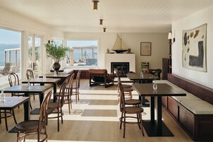 Un comedor amplio con varias mesas y sillas, una chimenea y un gran ventanal con vistas al exterior.