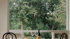 Una habitación con dos sillas de madera, una mesa y vistas a un bosque por la ventana.