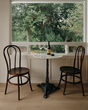 A room with two wooden chairs, a table, and a view of a forest through a window. - The Herondale Hotel (Astoria)