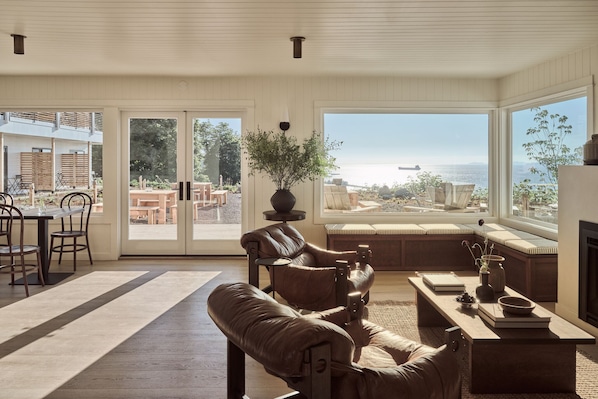 A spacious living room with a large window offering a view of the sea, a cozy seating area, and a fireplace. - The Herondale Hotel (Astoria)