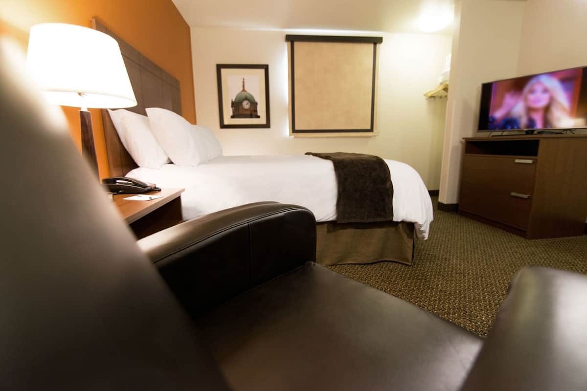 A hotel room with a bed, a desk with a lamp, a television, and a framed picture on the wall.