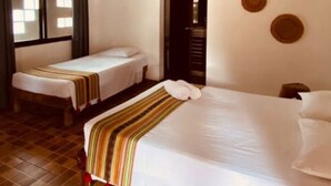 A hotel room with two single beds, a large bed, a window with curtains, an air conditioning unit, and a wall with circular decorations. - L´hotelito (Tulum)