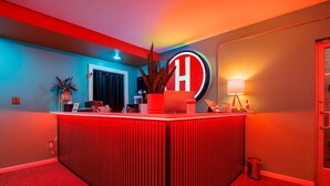 Een receptiegedeelte met een kleurenschema in rood en blauw, een groot ‘H’-bord, een receptiebalie, een potplant, een prullenbak en een lamp.