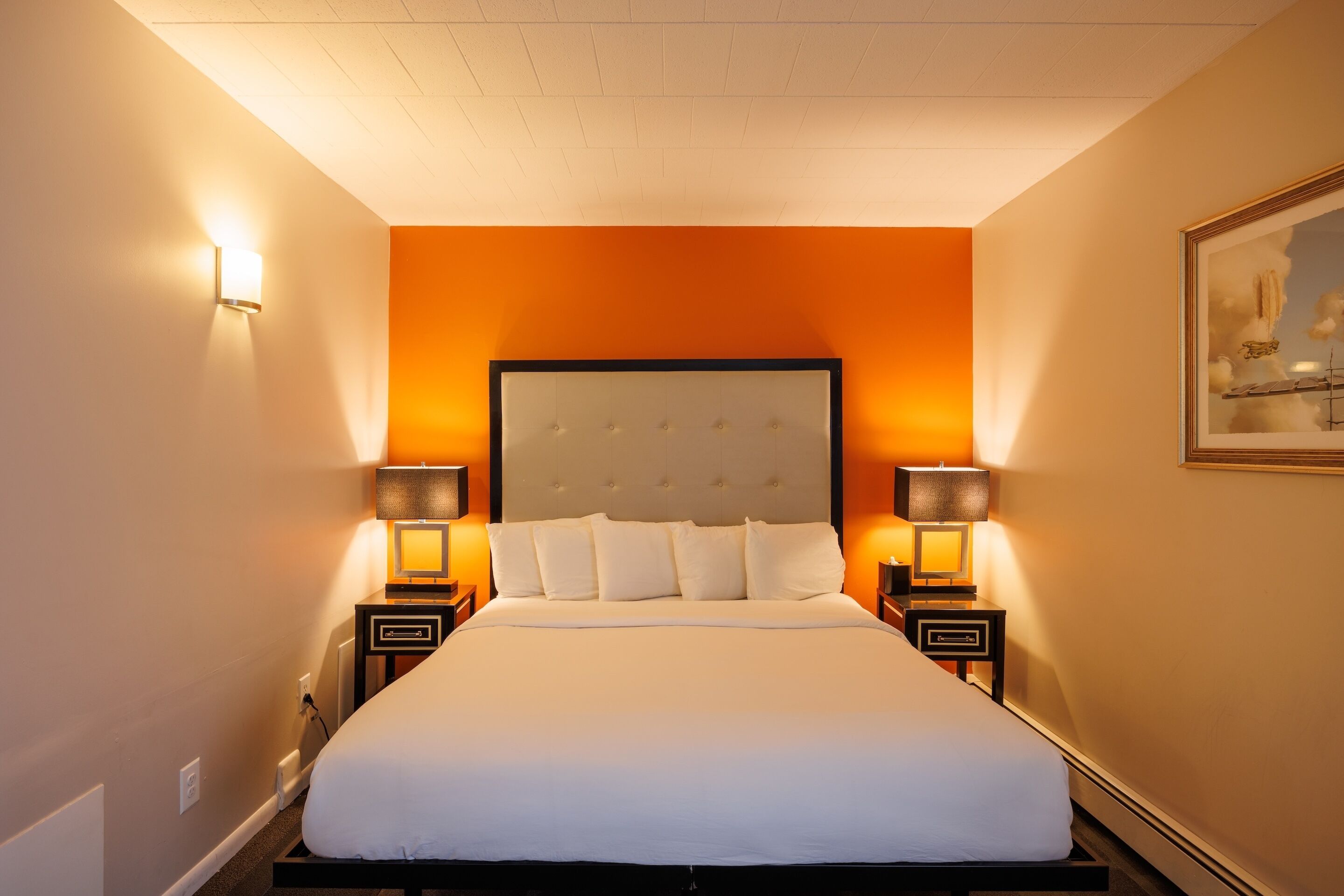 Una habitación de hotel con una cama grande, dos mesitas de noche con lámparas y un cuadro en la pared.
