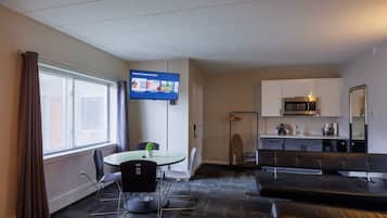 Ein modernes Hotelzimmer mit einem runden Esstisch, schwarzen Stühlen, einem Flachbildfernseher, einer Küchenzeile und einer Sitzecke mit einer Couch und einer Bank.