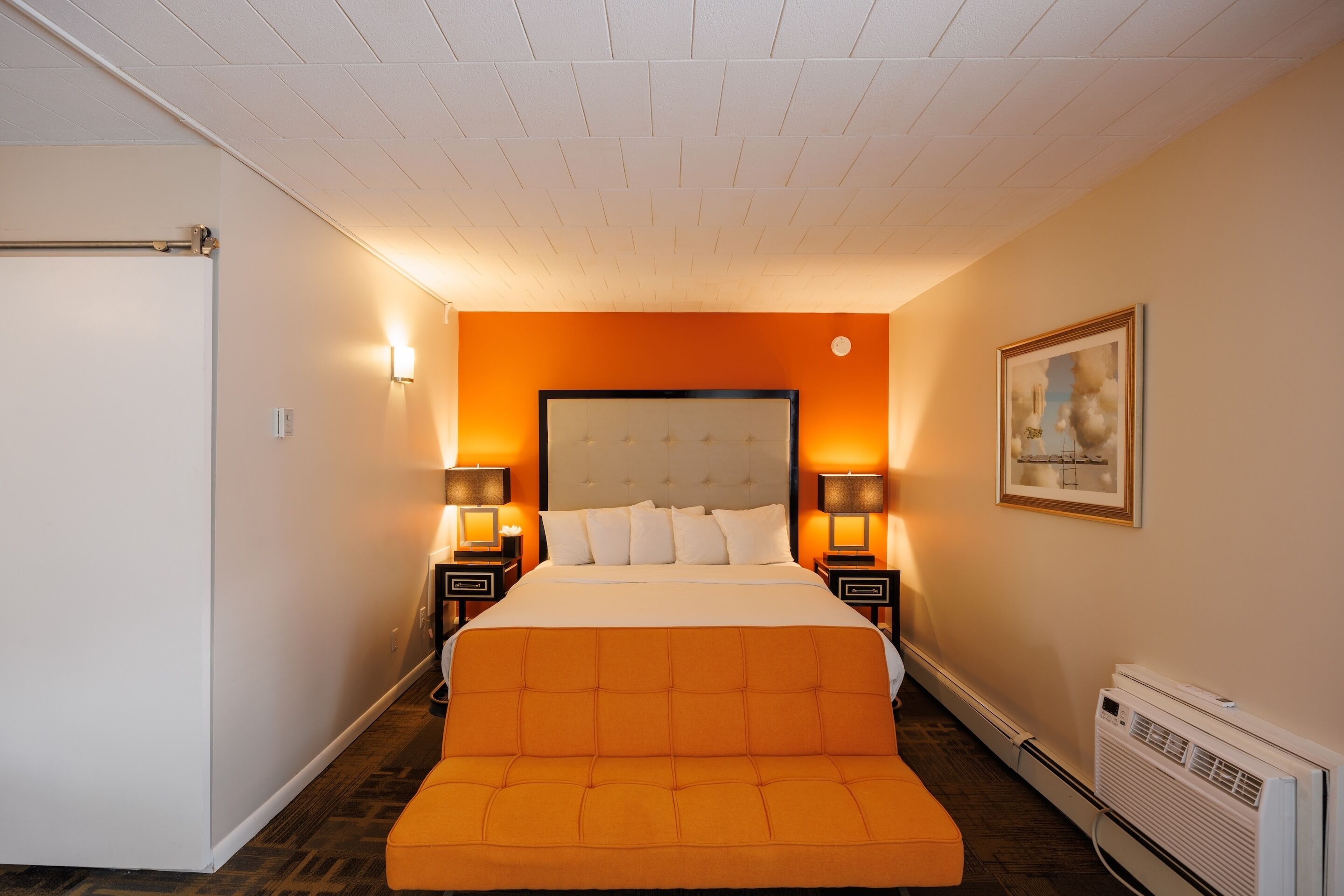 Una camera d'albergo con un letto grande, due lampade sui comodini, una testiera e un quadro appeso alla parete, oltre a un termosifone.