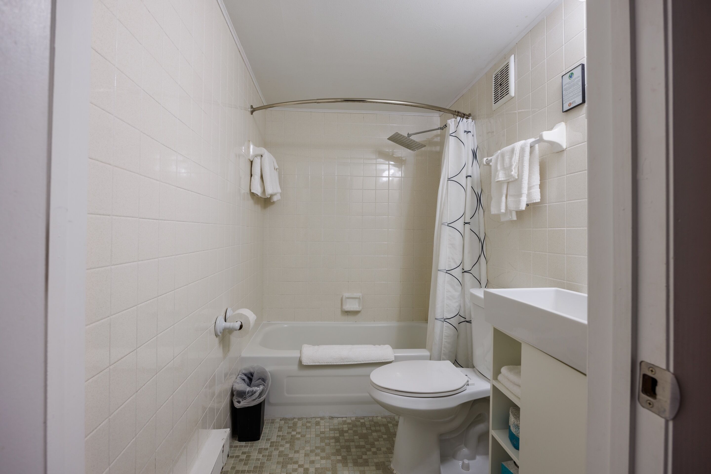 A small, clean bathroom with a toilet, sink, and bathtub. There are towels hanging on the wall and a shower curtain.