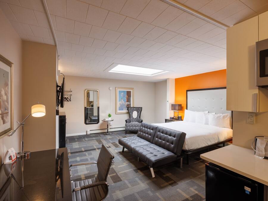 A hotel room with a bed, a sofa, a desk, a chair, a TV, and a minibar.