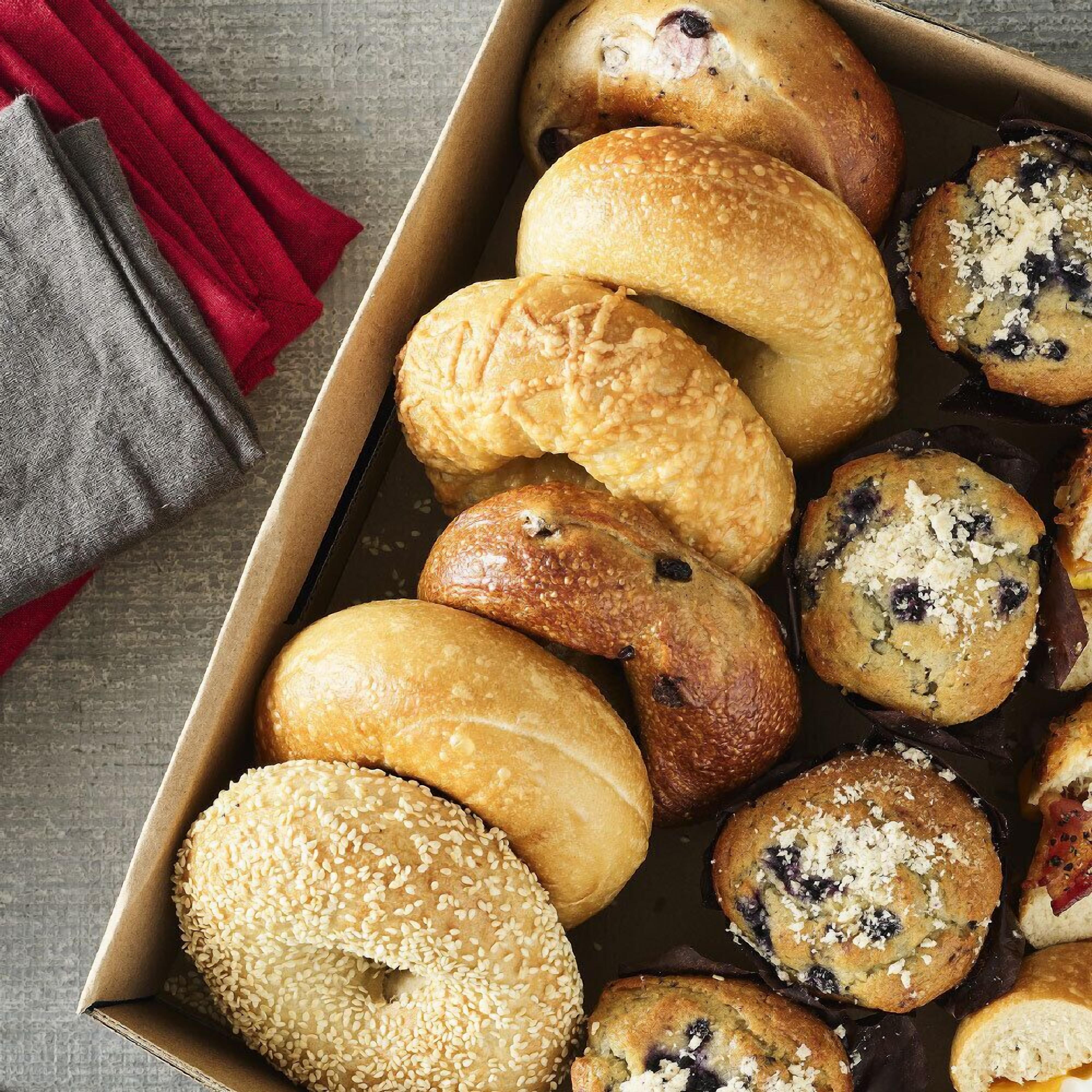 A variety of baked goods in a box, including bagels and muffins.