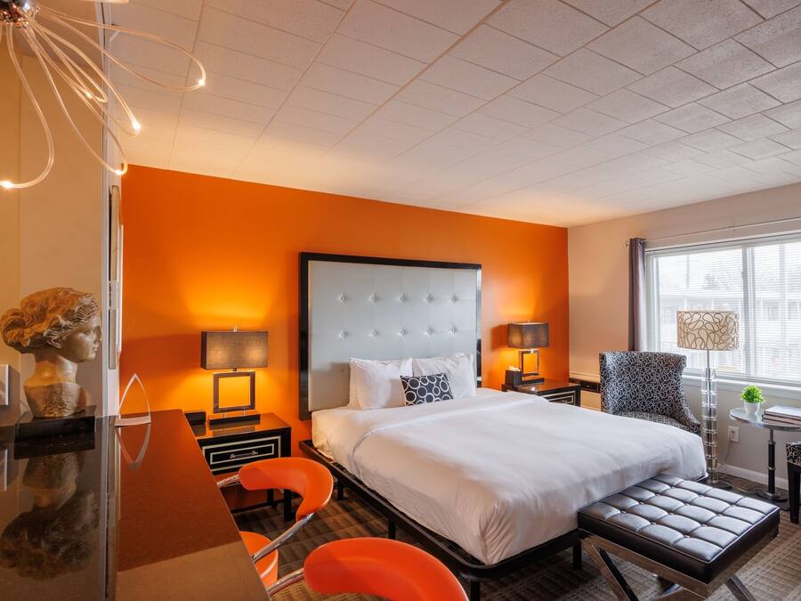 A hotel room with a large bed, two bedside tables with lamps, a desk with a chair, and a window with blinds.