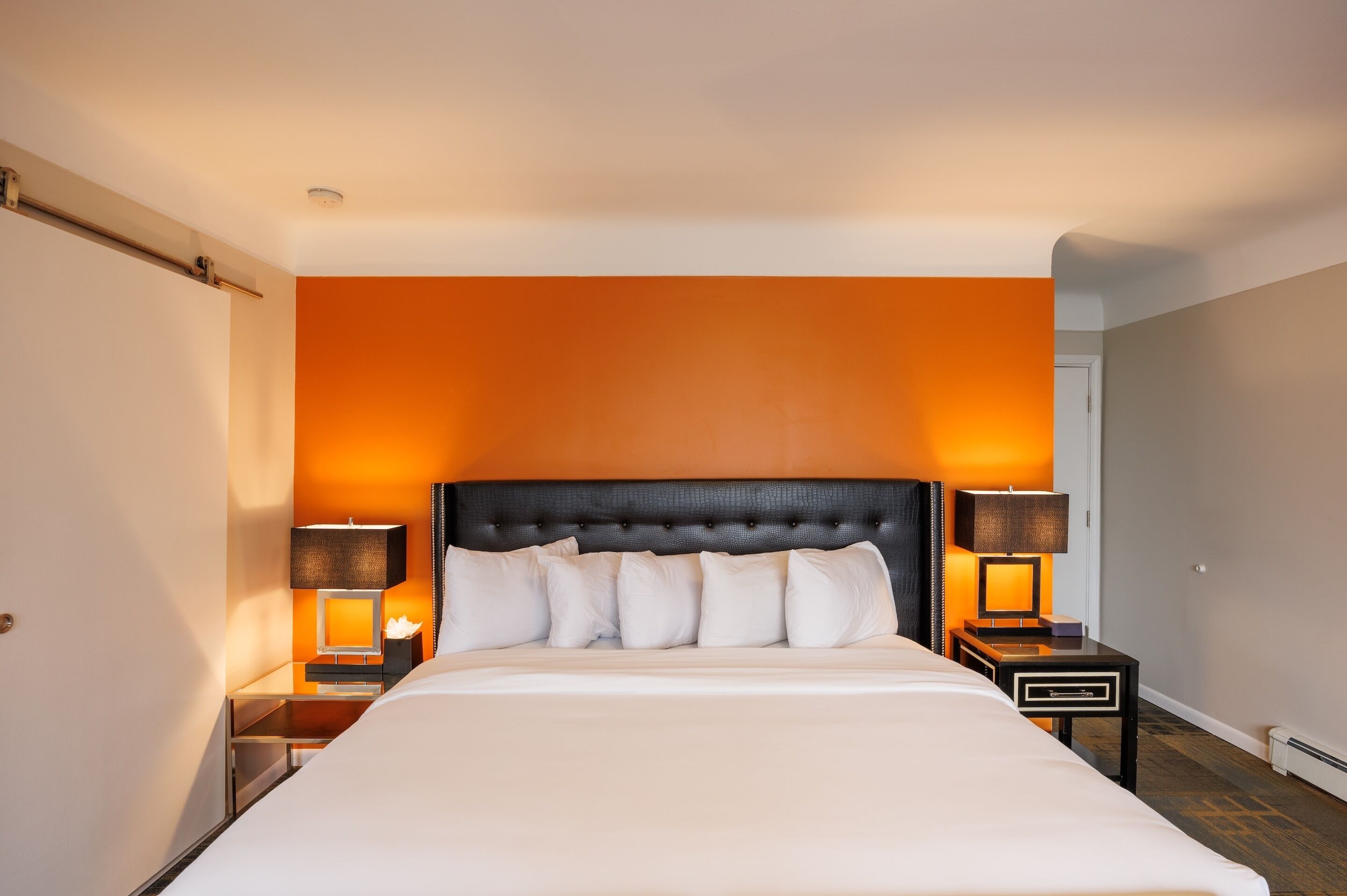 A hotel room with a large bed, two bedside tables with lamps, and an orange accent wall.