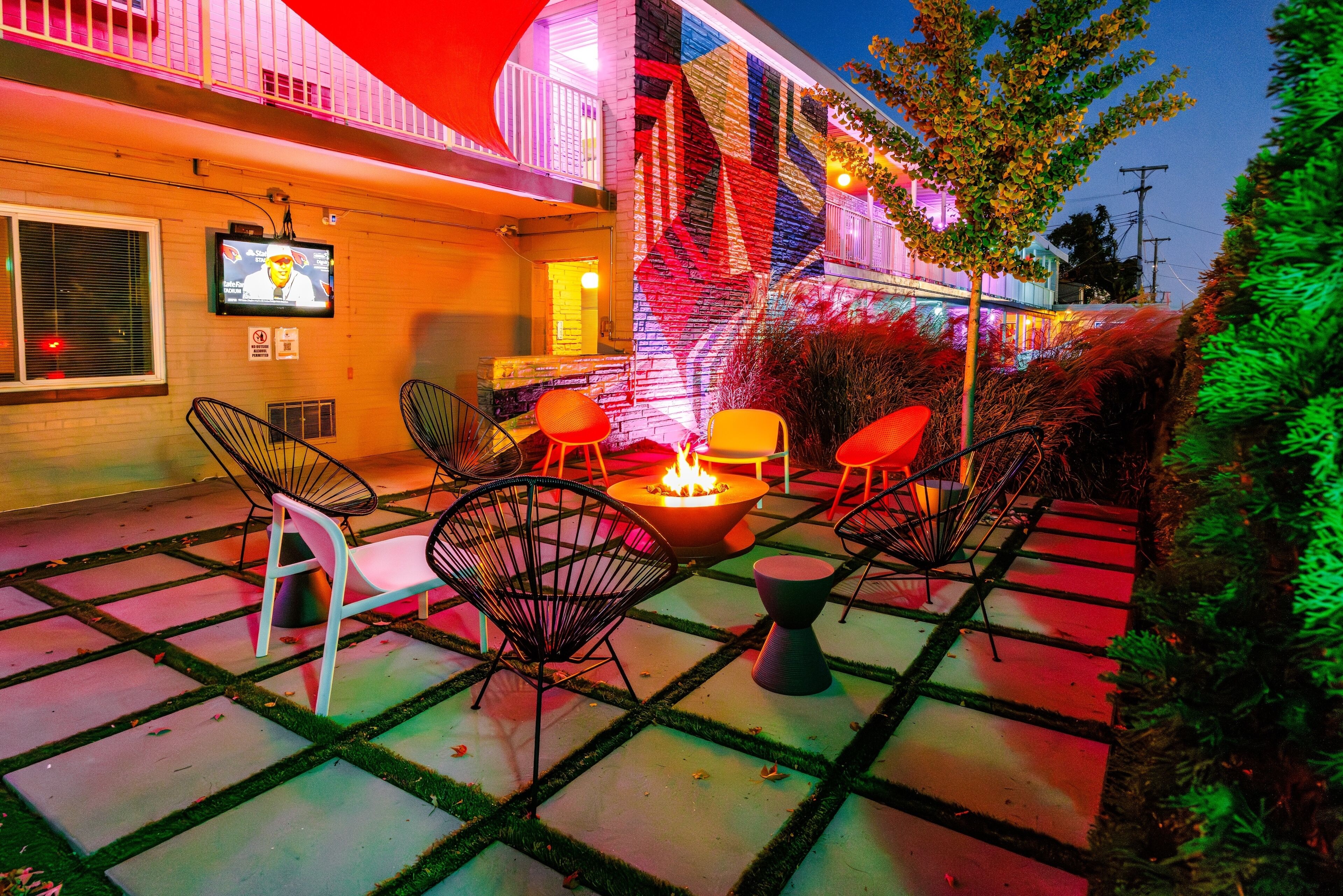 An outdoor patio with a fire pit, chairs, and a TV screen mounted on the wall.