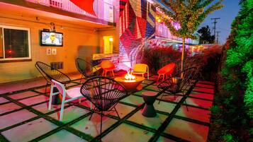 An outdoor patio with a fire pit, chairs, and a TV screen mounted on the wall.