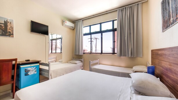 Ein Hotelzimmer mit zwei Einzelbetten, einem Schreibtisch mit Stuhl, einem Fernseher und einem Fenster mit Vorhängen.