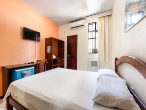 Une chambre d’hôtel avec un lit, un téléviseur fixé au mur, une armoire en bois et une fenêtre avec des rideaux.