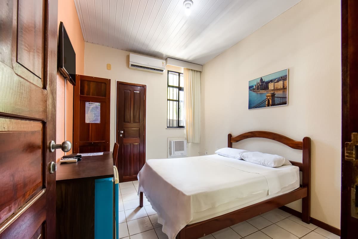 A hotel room with a wooden bed, a desk with a chair, a flat-screen TV, and a window with curtains.