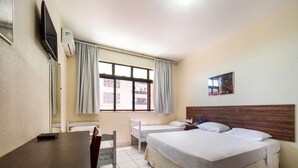 Ein Hotelzimmer mit einem Holztisch, zwei Einzelbetten, einem großen Fenster mit Vorhängen, einem flachbildfernseher an der Wand und einem Gemälde über dem Bett.