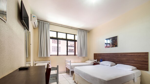 Une chambre d’hôtel avec un bureau en bois, deux lits simples, une grande fenêtre avec des rideaux, un téléviseur à écran plat fixé au mur et un tableau au-dessus du lit.