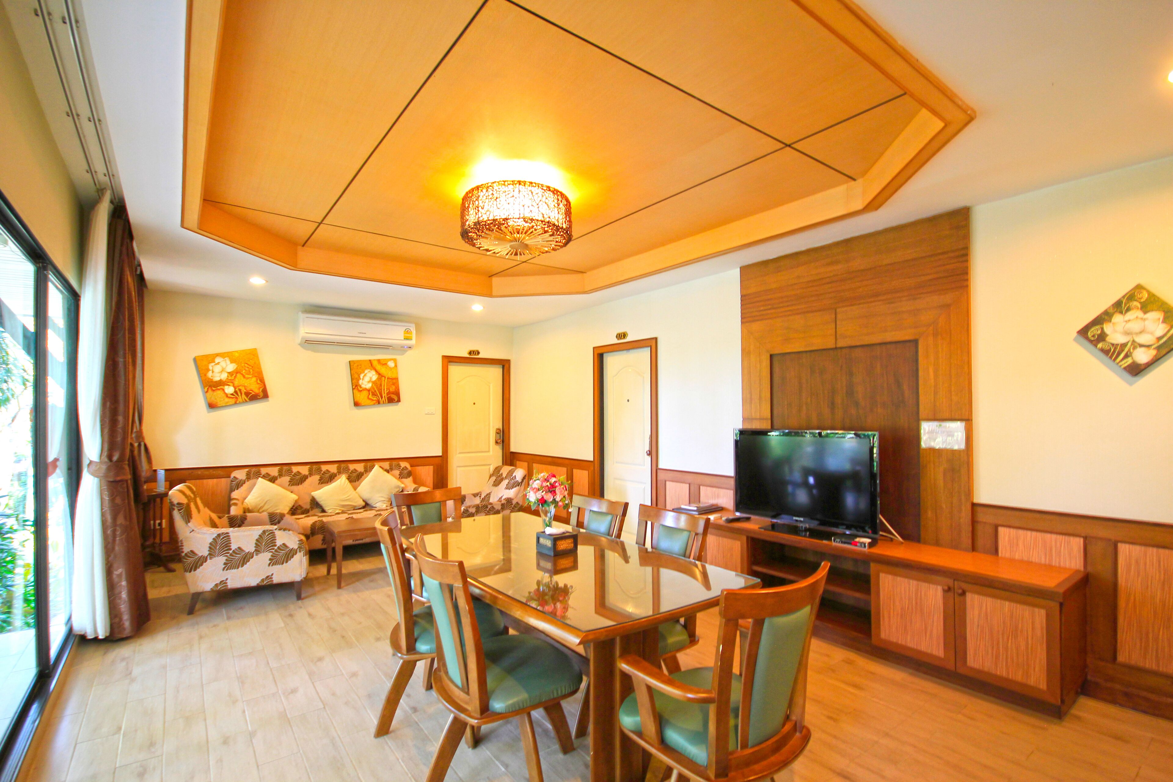 A dining area with a glass table, wooden chairs, a sofa, and a television.