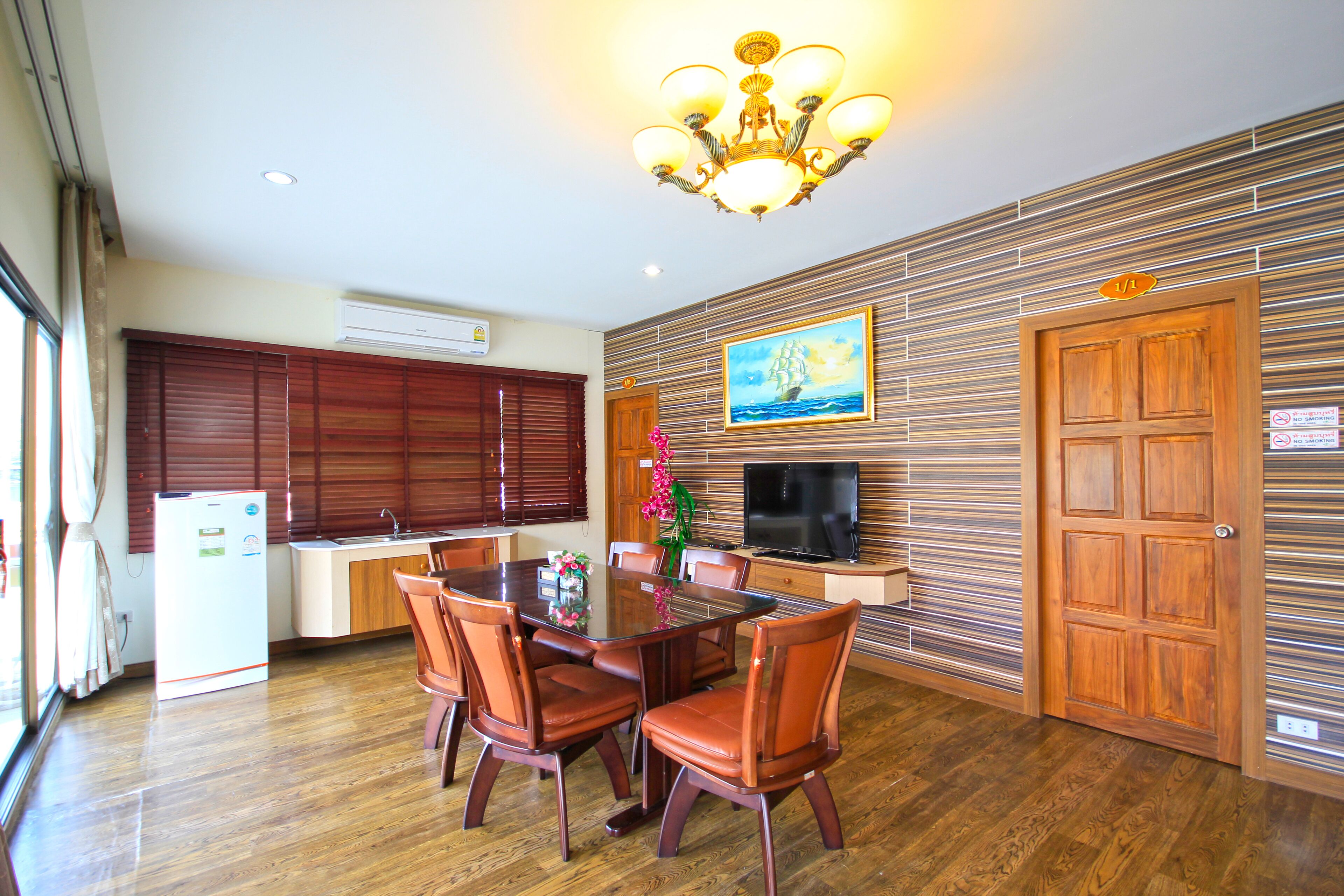 A modern kitchen with wooden cabinets, a dining table with chairs, a television, and a decorative painting on the wall.