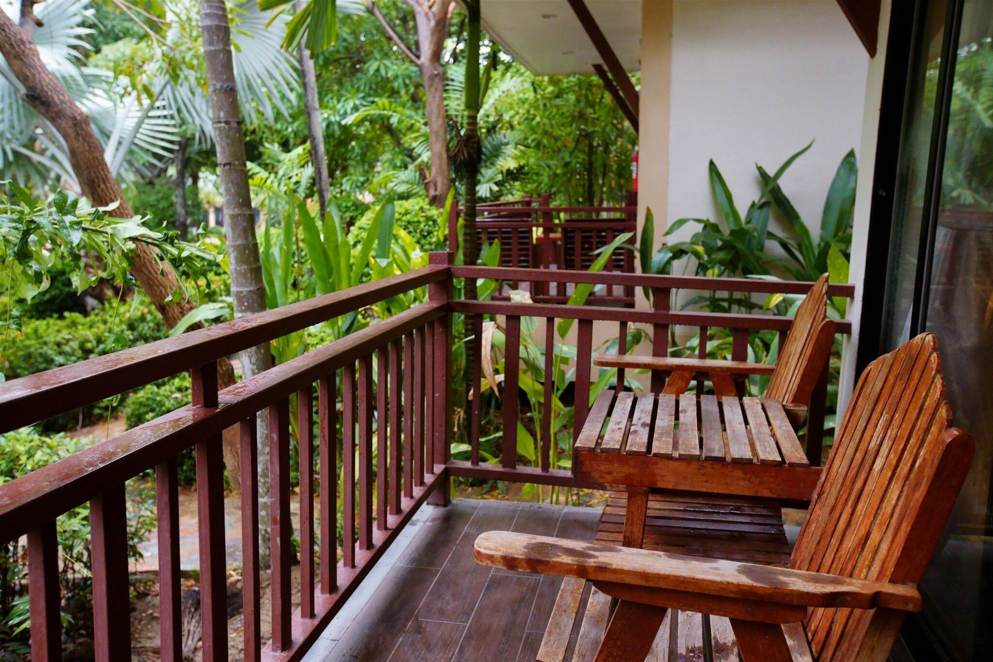 A wooden bench and table on a balcony with a view of lush greenery.