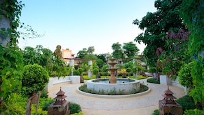 Ein Garten mit einer zentralen Fontäne, umgeben von Steinwegen und viel Grün.