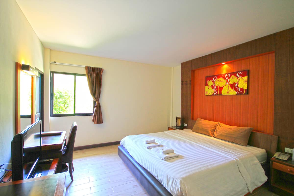 Habitación de hotel con cama, escritorio, silla, ventana con cortinas, un cuadro en la pared y mesita de noche con teléfono.