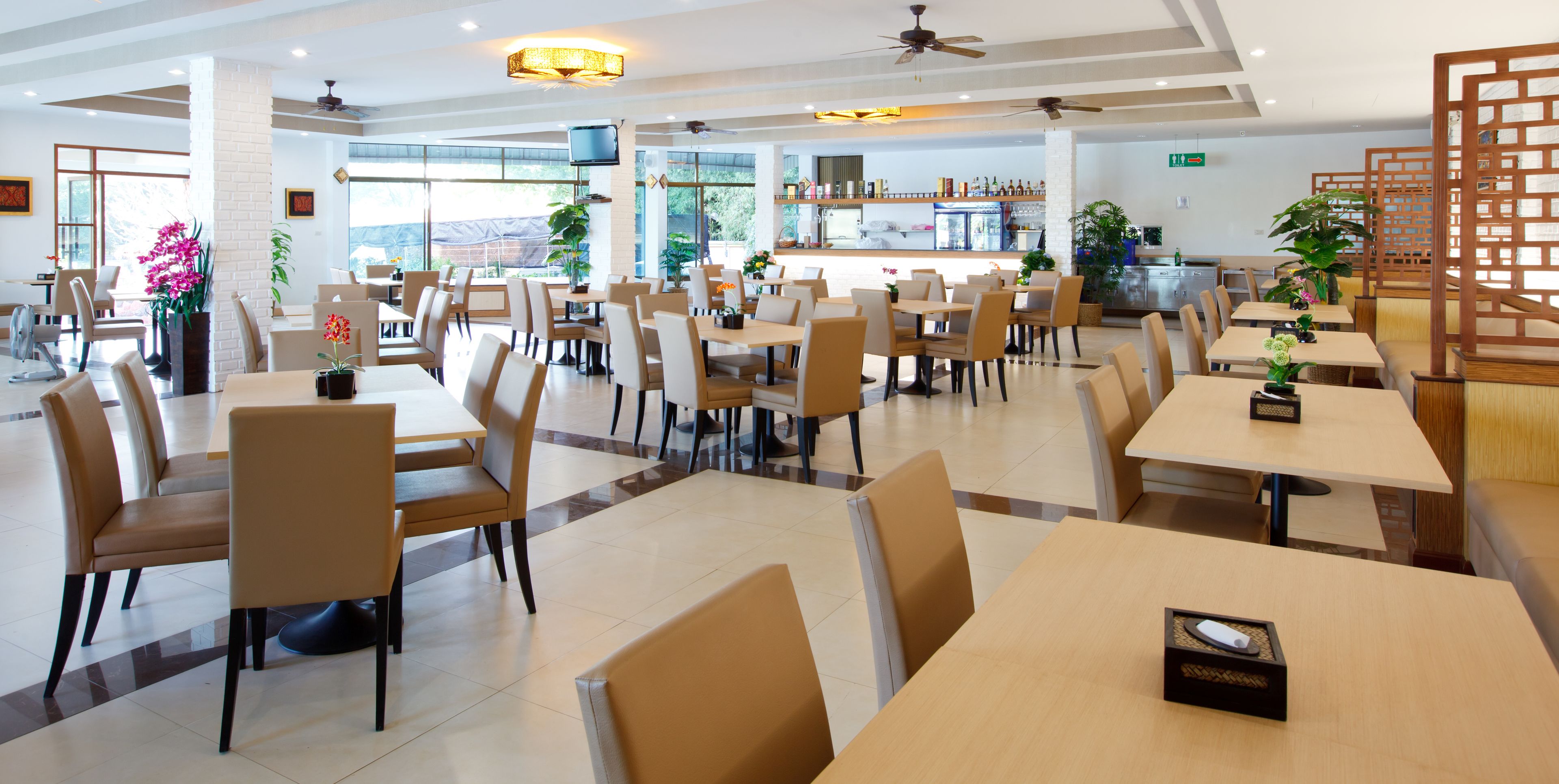 Un comedor amplio con varias mesas y sillas, una barra al fondo y ventanas grandes que dejan entrar luz natural.