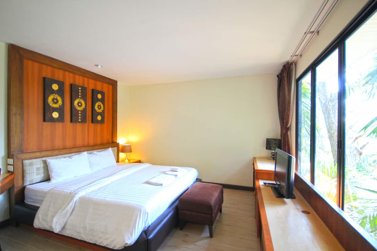 Habitación de hotel con una cama grande, un escritorio con computadora, una ventana con vistas a la vegetación y decoración en la pared.