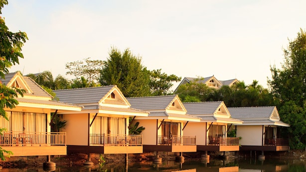Eine Reihe von Bungalows auf Stelzen, mit Balkonen, deren Spiegelung sich im Wasser zeigt.