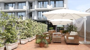 A modern outdoor seating area with white umbrellas, wicker furniture, and potted plants. - Hotel Barbarella (Giugliano in Campania)
