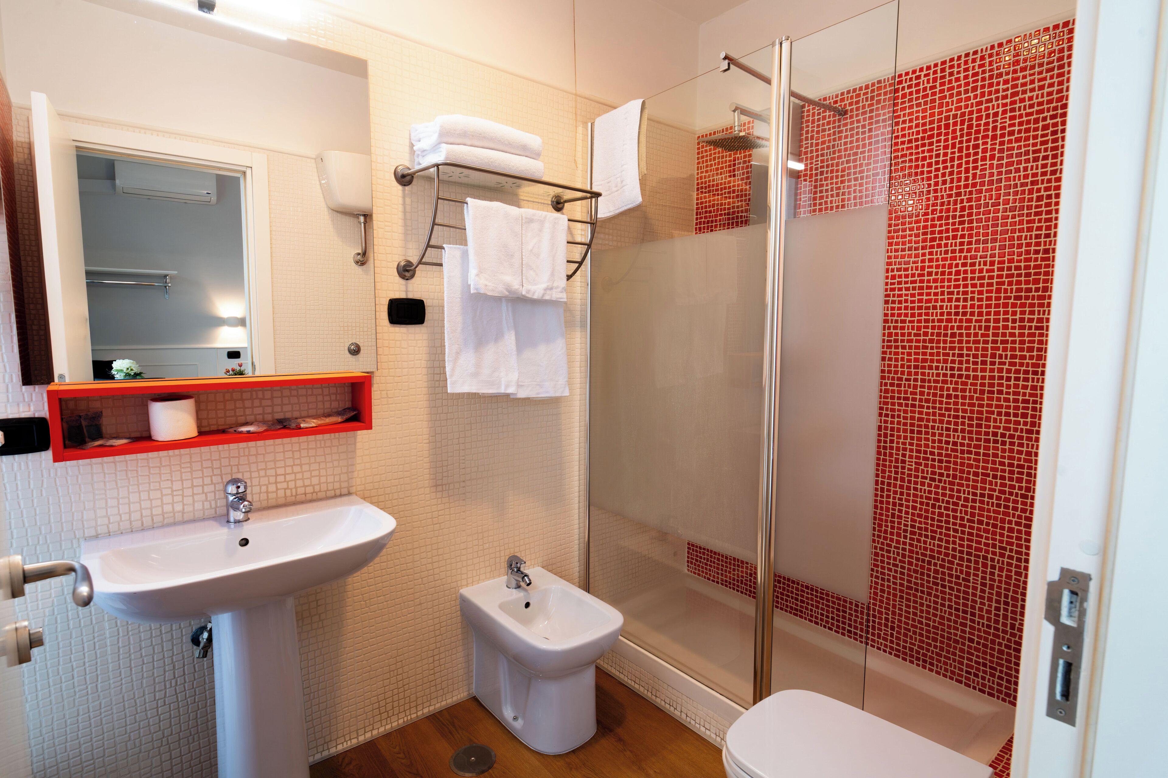 Een moderne badkamer met een douchecabine van glas, een bidet, een wastafel en een spiegel.