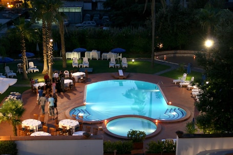 A pool area with lounge chairs, umbrellas, and tables, surrounded by palm trees and greenery.