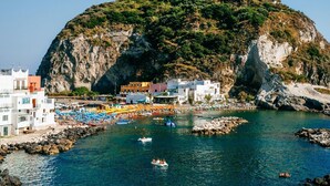 A coastal town with a rocky hill, clear blue water, and colorful buildings. - Hotel Barbarella (Giugliano in Campania)