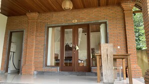 A brick building with a large glass door, a wooden ceiling, and a small wooden table outside. - Bagiya Suites & Villas (Ubud)