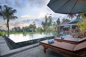A poolside area with lounge chairs, a statue, and a view of palm trees and a building in the background.