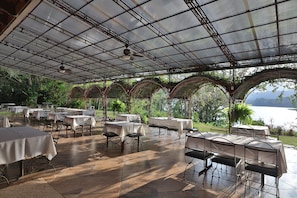 An outdoor covered dining area with tables and chairs, a ceiling fan, and a view of a body of water. - La Casona del Cafetal (Cachi)