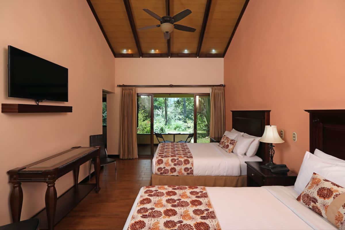 A hotel room with two beds, a television, a desk, and a view of the outdoors.