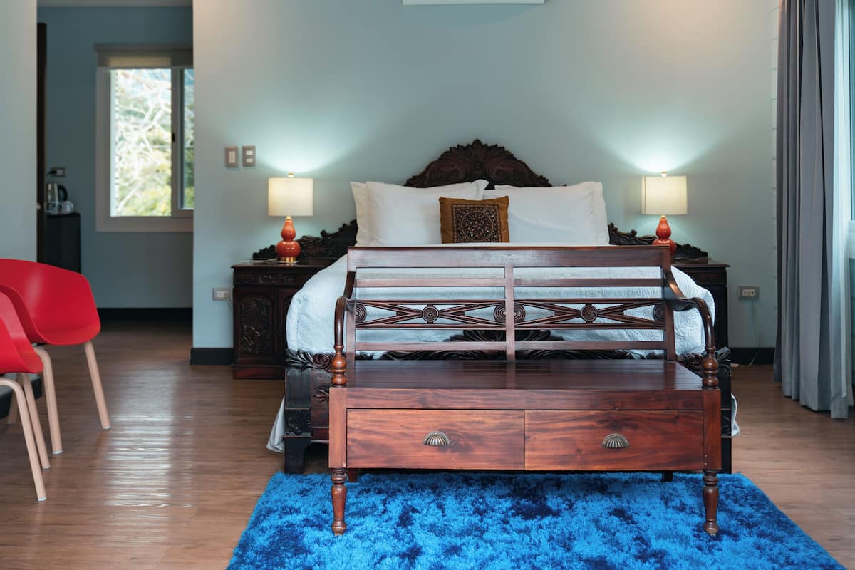 A bedroom with a wooden bed, two bedside lamps, a nightstand, a red chair, and a blue rug.