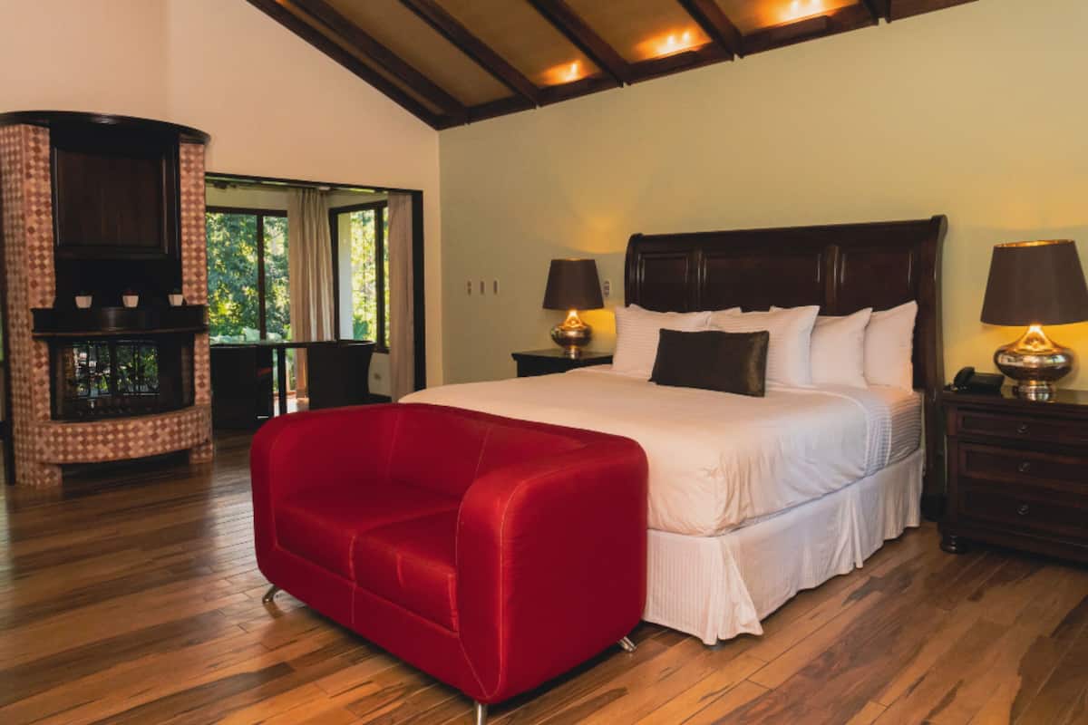 A bedroom with a large bed, a red sofa, wooden flooring, and a fireplace.