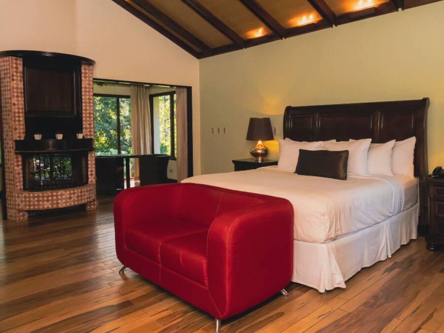 A bedroom with a large bed, a red sofa, wooden flooring, and a fireplace.
